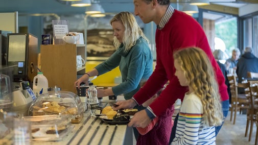 Mother, father and child paying at the cafe counter at Sizergh. They have a tray with two scones and a piece of cake.